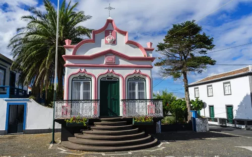 Kleine Kapelle mit rosa Details und Palmen im Hintergrund an einem sonnigen Tag.