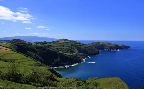 Küstenlandschaft mit Klippen, grünem Land und blauem Meer unter klarem Himmel.