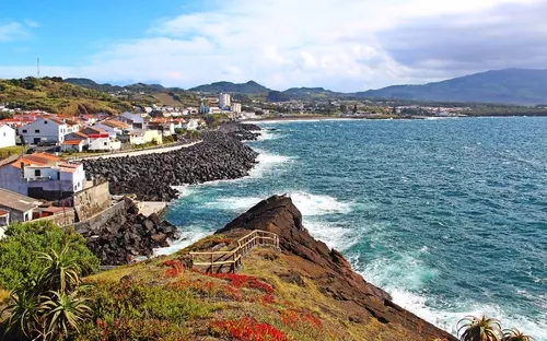 Küstenlandschaft mit Häusern, Meer und Bergen im Hintergrund.