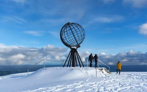 Menschen stehen bei winterlicher Aussicht an der Nordkapp-Globe-Skulptur in Norwegen.