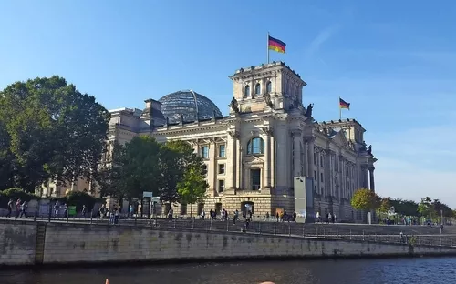 Reichstagsgebäude in Berlin mit deutscher Flagge bei blauem Himmel.