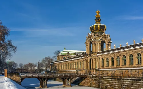 Historisches Gebäude mit goldener Krone, verschneite Umgebung, blauer Himmel.