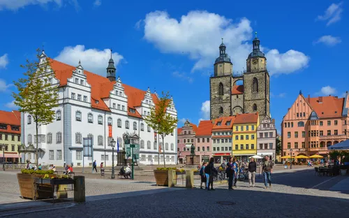 Historischer Marktplatz mit alten Gebäuden und Menschen unter blauem Himmel.