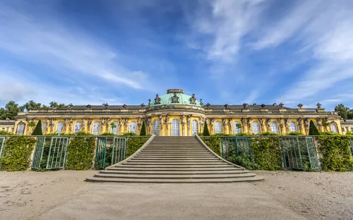 Schloss Sanssouci mit breiter Treppe und blauem Himmel im Hintergrund.