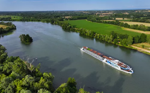 Kreuzfahrtschiff auf einem Fluss, umgeben von grüner Landschaft.