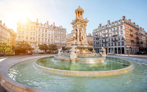 Brunnen auf einem Platz mit historischen Gebäuden im Hintergrund bei Sonnenschein.