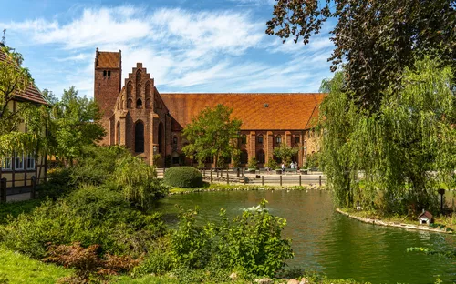 Kirche am See mit roten Ziegeln und grüner Parklandschaft bei sonnigem Wetter