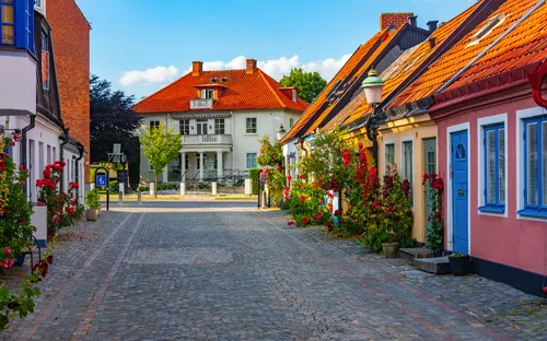 Pflasterstraße mit bunten Häusern und Rosen in einer malerischen Stadt.