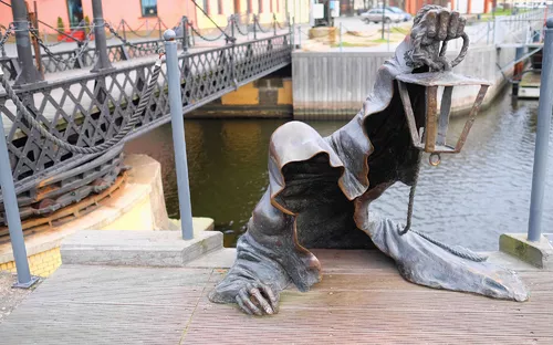 Skulptur eines verhexten Mannes, der eine Laterne hält, bei einer Brücke.