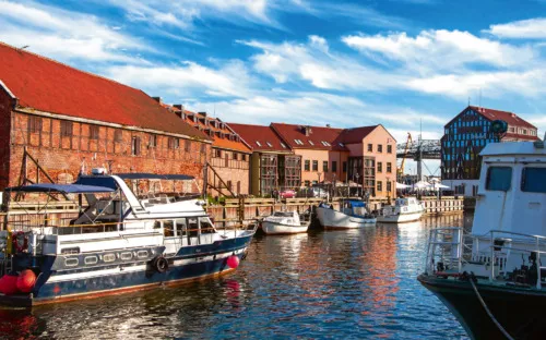 Boote im historischen Hafen vor alten Backsteingebäuden bei blauem Himmel.