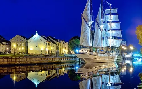 Segelschiff im Hafen bei Nacht, reflektiert im ruhigen Wasser.