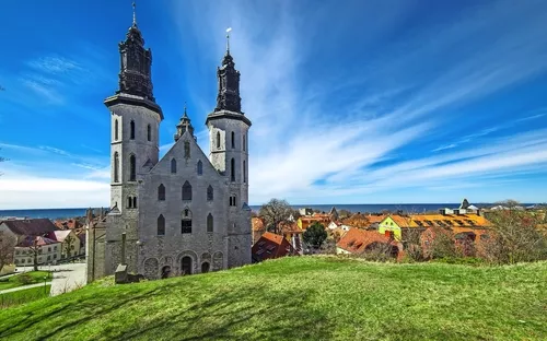 Kirche mit zwei Türmen auf einem Hügel vor blauem Himmel und Dorf im Hintergrund.