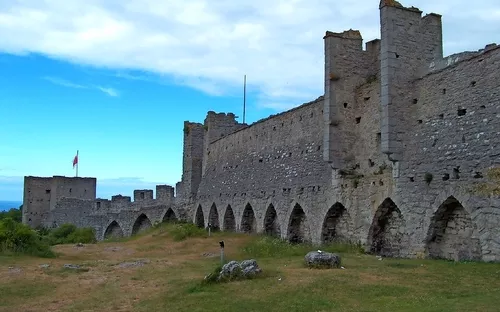 Alte Steinmauer einer Festung mit Türmen unter leicht bewölktem Himmel.