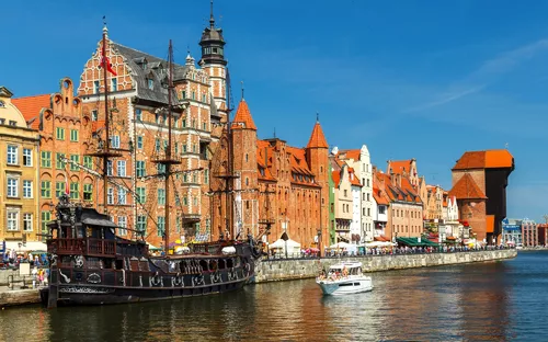 Stadtansicht von Danzig mit historischem Schiff und Backsteingebäuden am Flussufer.