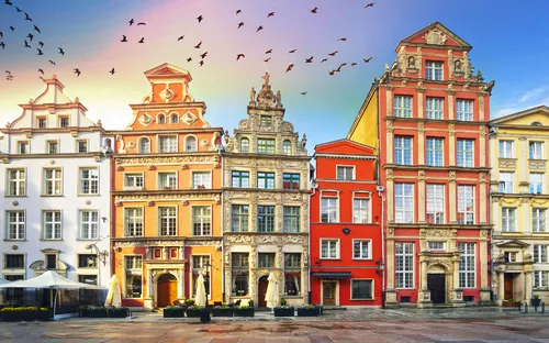 Historische Gebäude am zentralen Platz mit vorbeifliegenden Vögeln im Himmel.