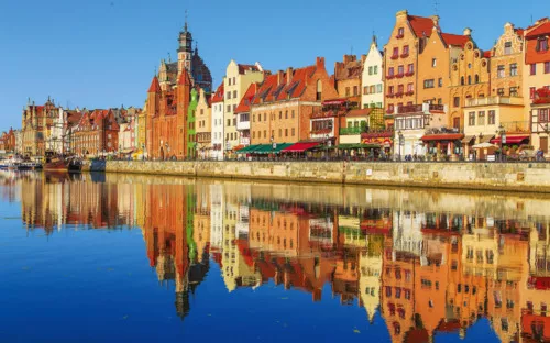 Bunte Häuserzeile spiegelt sich im Wasser eines Flusses.