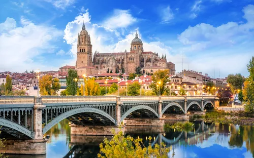Brücke und Kathedrale in Salamanca bei Tageslicht, reflektiert im Wasser.