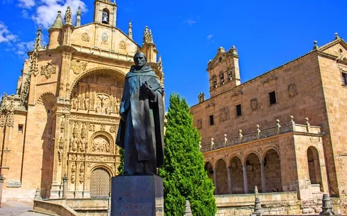 Statue vor historischer Kirche mit reicher Fassade und blauem Himmel.