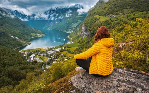 Person auf Felsen blickt auf Fjord und Berglandschaft.
