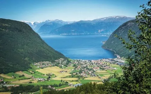 Blick auf ein Tal mit Dorf, umgeben von Bergen und einem See im Hintergrund.