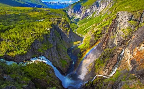 Wasserfall in einer beeindruckenden Berglandschaft mit Regenbogen im Tal.