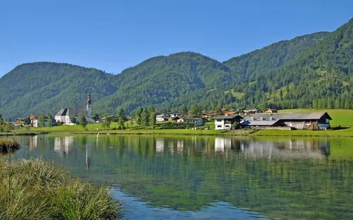 Landschaft mit Dorf am See, umgeben von grünen Bergen.