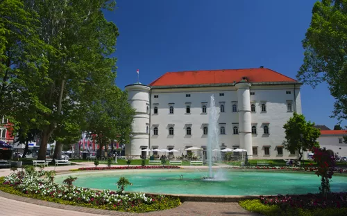 Historisches Gebäude mit Springbrunnen und Gartenanlage bei sonnigem Wetter.