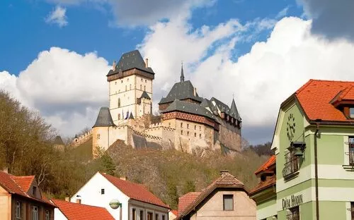 Burg auf einem Hügel mit umliegenden Gebäuden und bewölktem Himmel.