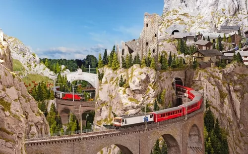 Eisenbahn fährt über Brücke in alpiner Landschaft mit Bergen und Bäumen.