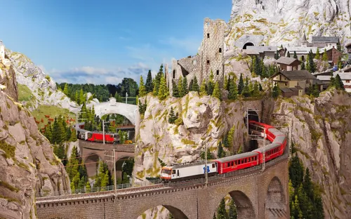 Eisenbahn fährt über Brücke in alpiner Landschaft mit Bergen und Bäumen.
