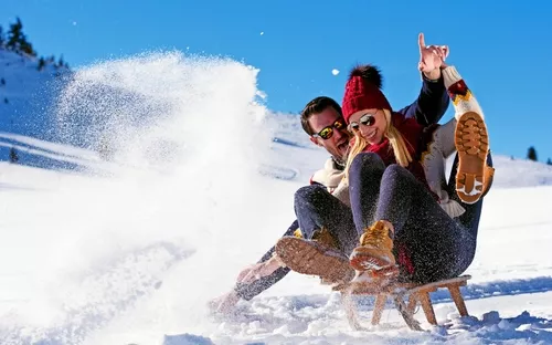 Paar hat Spaß beim Schlittenfahren im Schnee an einem sonnigen Wintertag