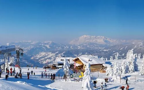 Verschneites Skigebiet mit Skifahrern auf einem Gipfelplateau und Bergpanorama im Hintergrund.