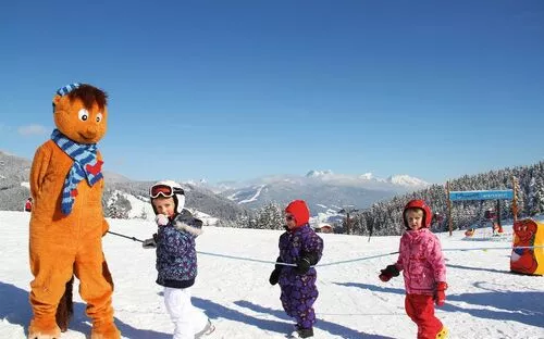 Kinder mit Maskottchen in schneebedeckter Wagrainis Winterwelt, klare Sicht auf Berge.