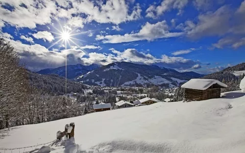 Verschneite Landschaft mit Hütten und Bergen im Sonnenlicht.