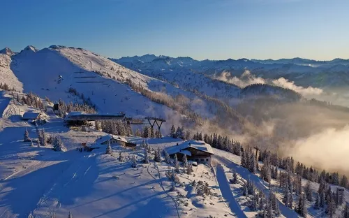 Verschneites Alpenpanorama mit Hütten und Liftanlagen im Sonnenlicht.