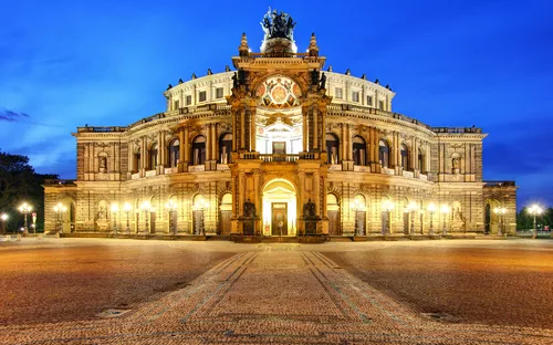 Historisches Opernhaus bei Abenddämmerung, beleuchtet vor blauem Himmel.