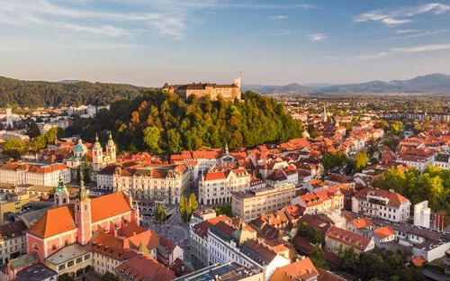 Luftaufnahme einer europäischen Stadt mit Burg auf einem Hügel im Hintergrund.