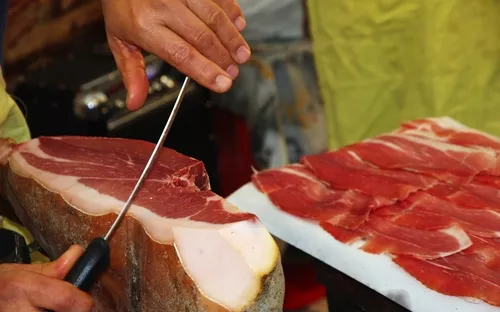 Eine Person schneidet Schinken in dünne Scheiben.