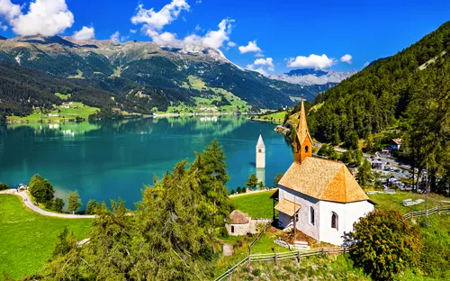 Kirche und halbversunkener Kirchturm an einem See in den Alpen.
