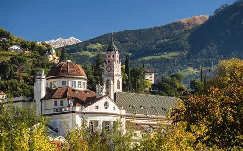 Kirchturm und Gebäude vor Alpenlandschaft im Herbstlicht