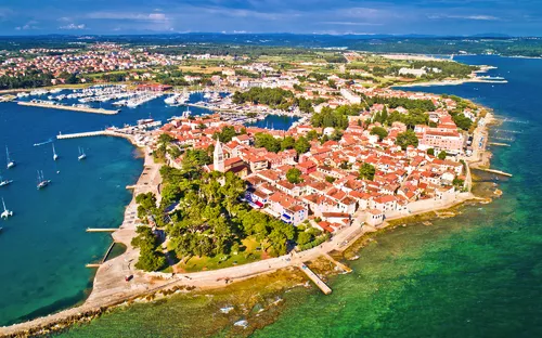 Luftaufnahme eines Küstenstädtchens mit roten Dächern und grünem Wasser.