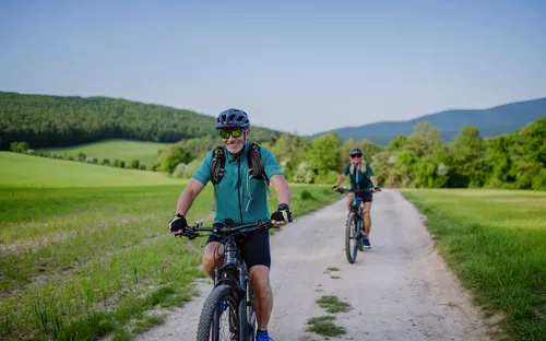 Zwei Fahrradfahrer auf einem Feldweg in einer grünen Landschaft.