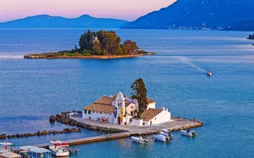Kloster auf Insel im Meer mit Bergkulisse bei Sonnenuntergang.