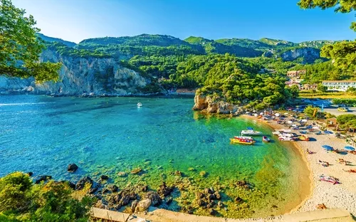 Strandbucht mit klarem Wasser, grünen Hügeln und Menschen beim Sonnenbaden.