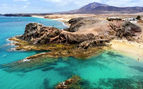 Küste mit Felsen und türkisfarbenem Meer auf einer sonnigen Insel.