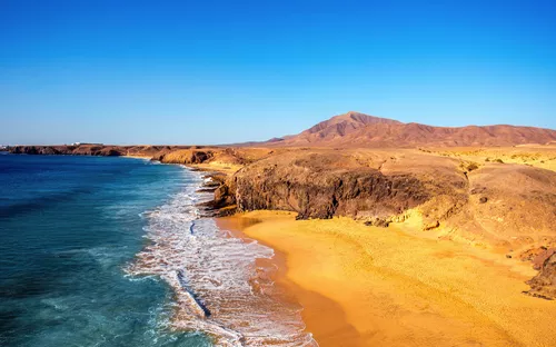 Küste mit goldenem Sand und blauem Meer unter klarem Himmel.