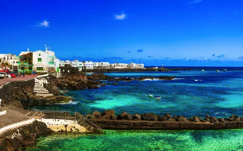 Panoramablick auf eine Küstenstadt mit weißen Gebäuden, türkisfarbenem Wasser und blauem Himmel.