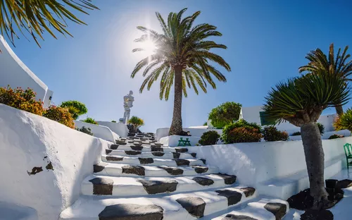 Steintreppe mit Palmen und weißen Wänden unter sonnigem Himmel.