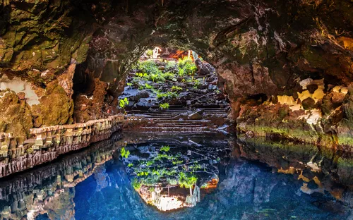 Unterirdische Höhle mit blauem Wasser und Pflanzen an den Felswänden.