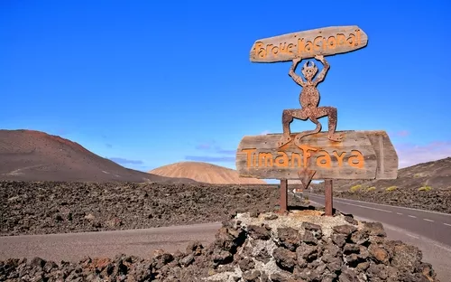 Steinige Landschaft im Timanfaya-Nationalpark mit hölzernem Eingangsschild.
